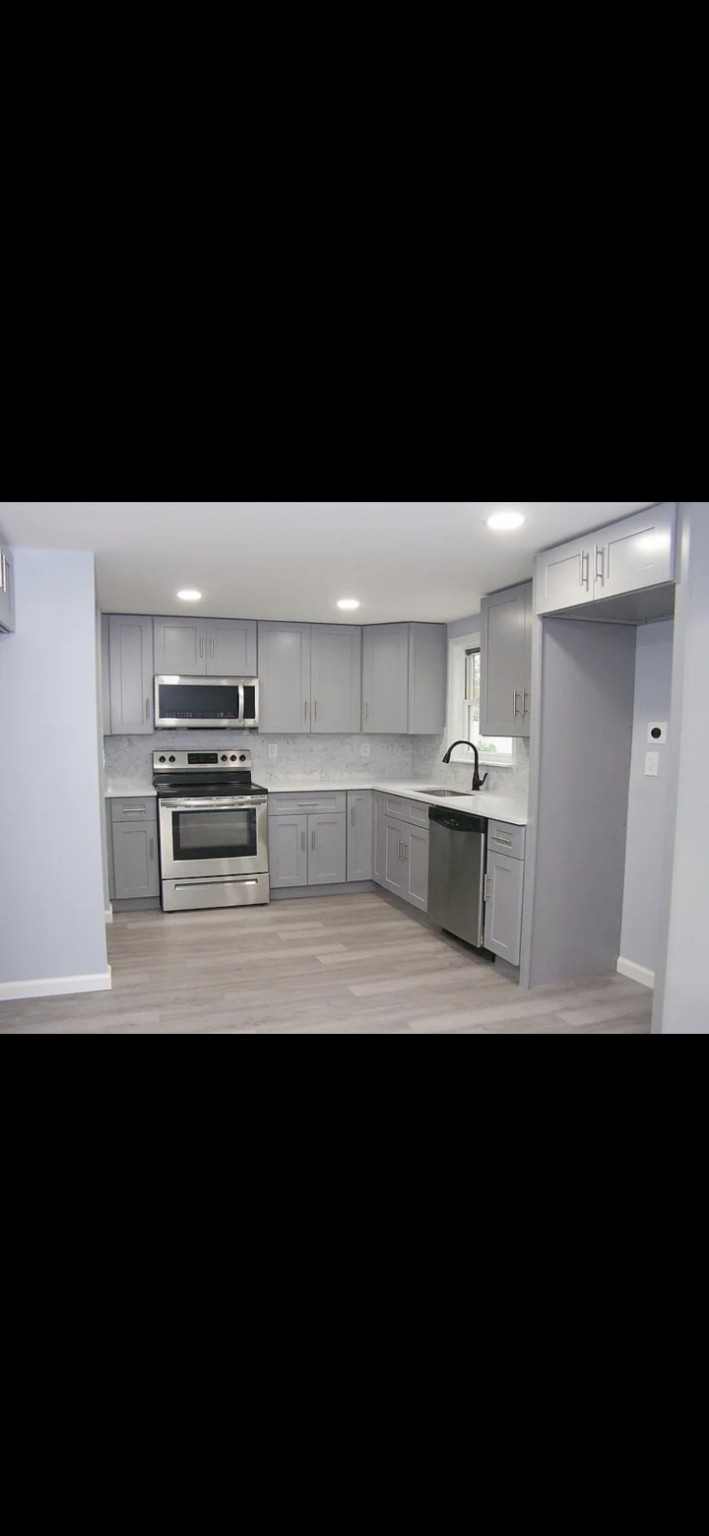 Completed light grey Shaker kitchen with quartz countertop and black hardware
