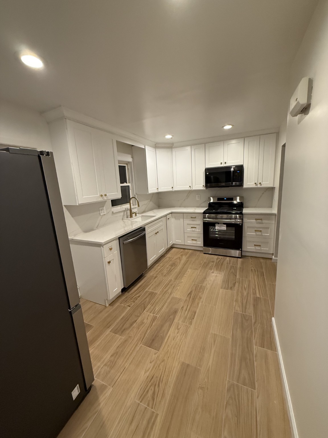 Completed white Shaker kitchen with quartz backsplash and wood-look flooring