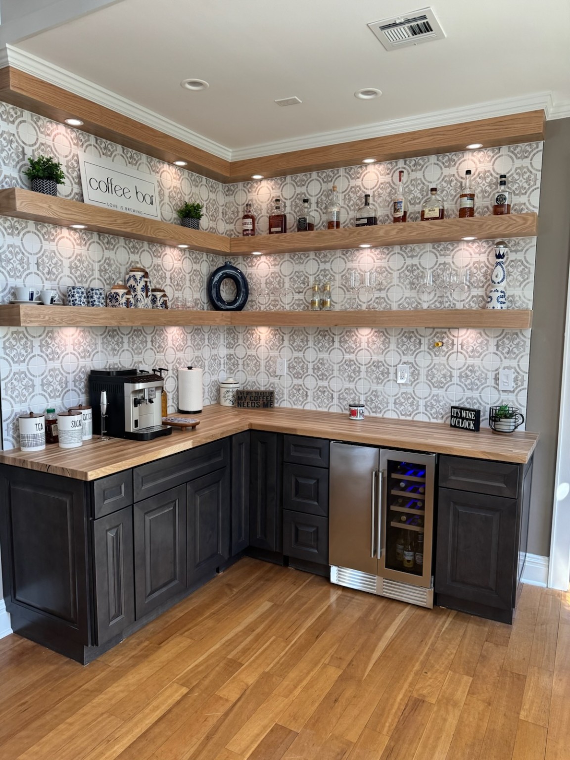 Completed custom coffee bar with dark cabinetry, wood countertops and floating shelves