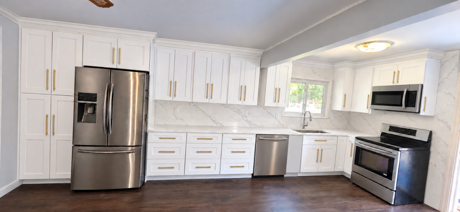 Completed white Shaker kitchen with gold hardware, full-height quartz backsplash and stainless appliances